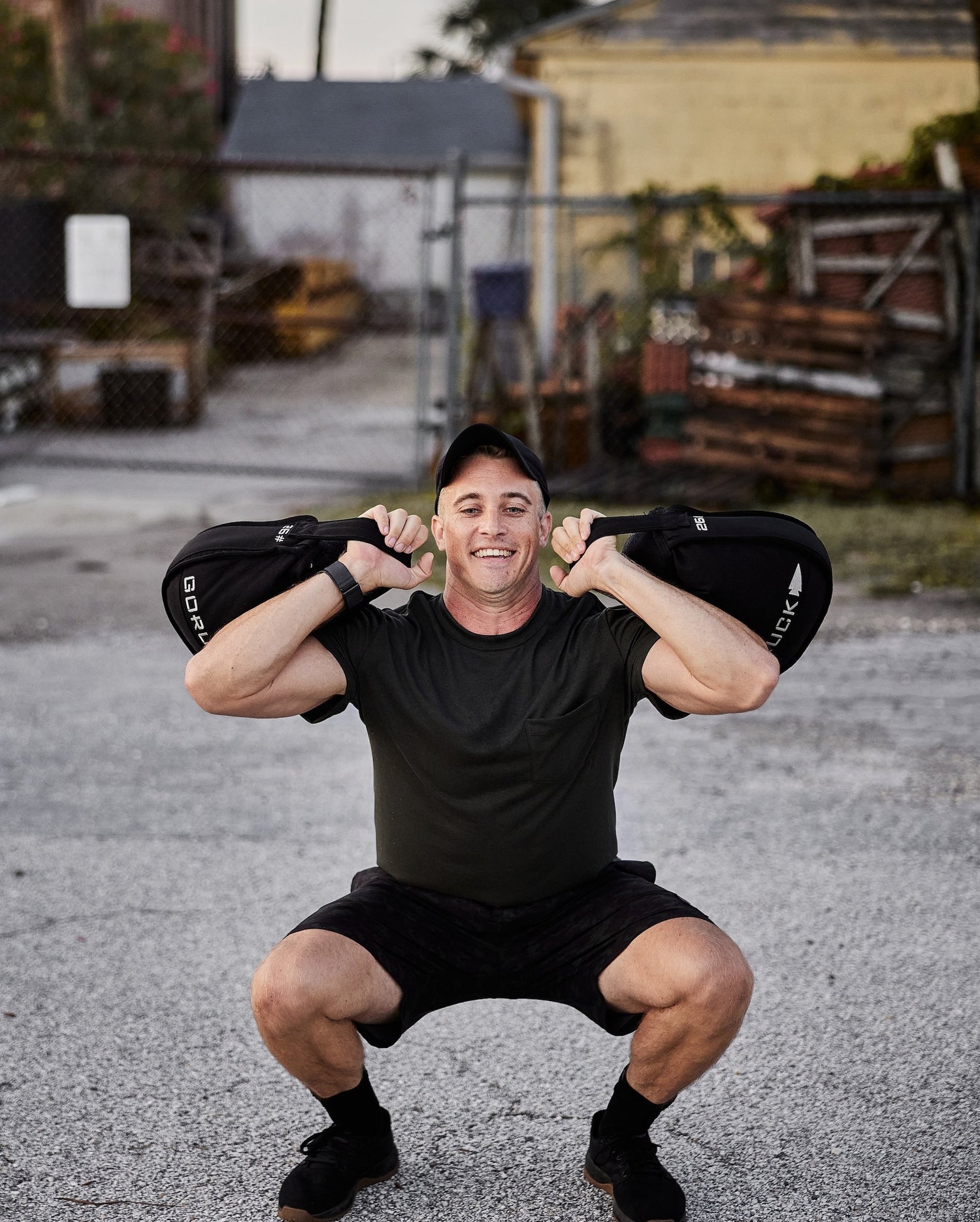 Man performing outdoor squat with GORUCK sandbags, wearing athletic gear, urban background