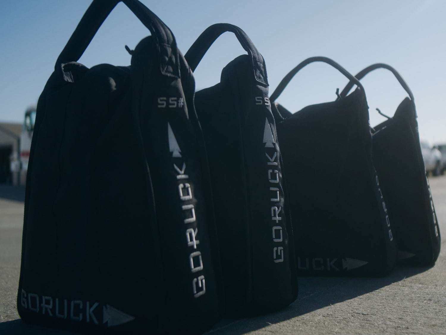 GORUCK rucking sandbags lined up outdoors on pavement in sunlight