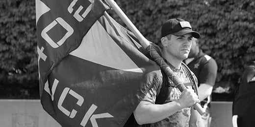 Man in GORUCK gear carrying large ruck flag outdoors during rucking event