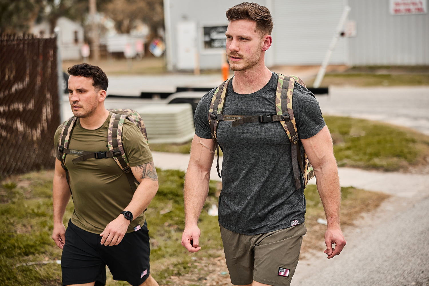Two men wearing GORUCK rucksacks walk outdoors in athletic gear, showcasing durable rucking backpacks