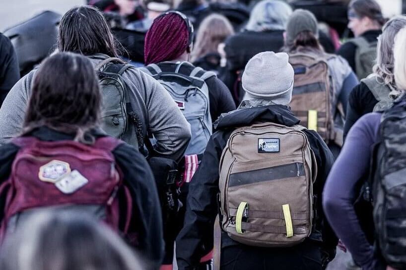 Group of people wearing GORUCK backpacks during outdoor rucking event, seen from behind