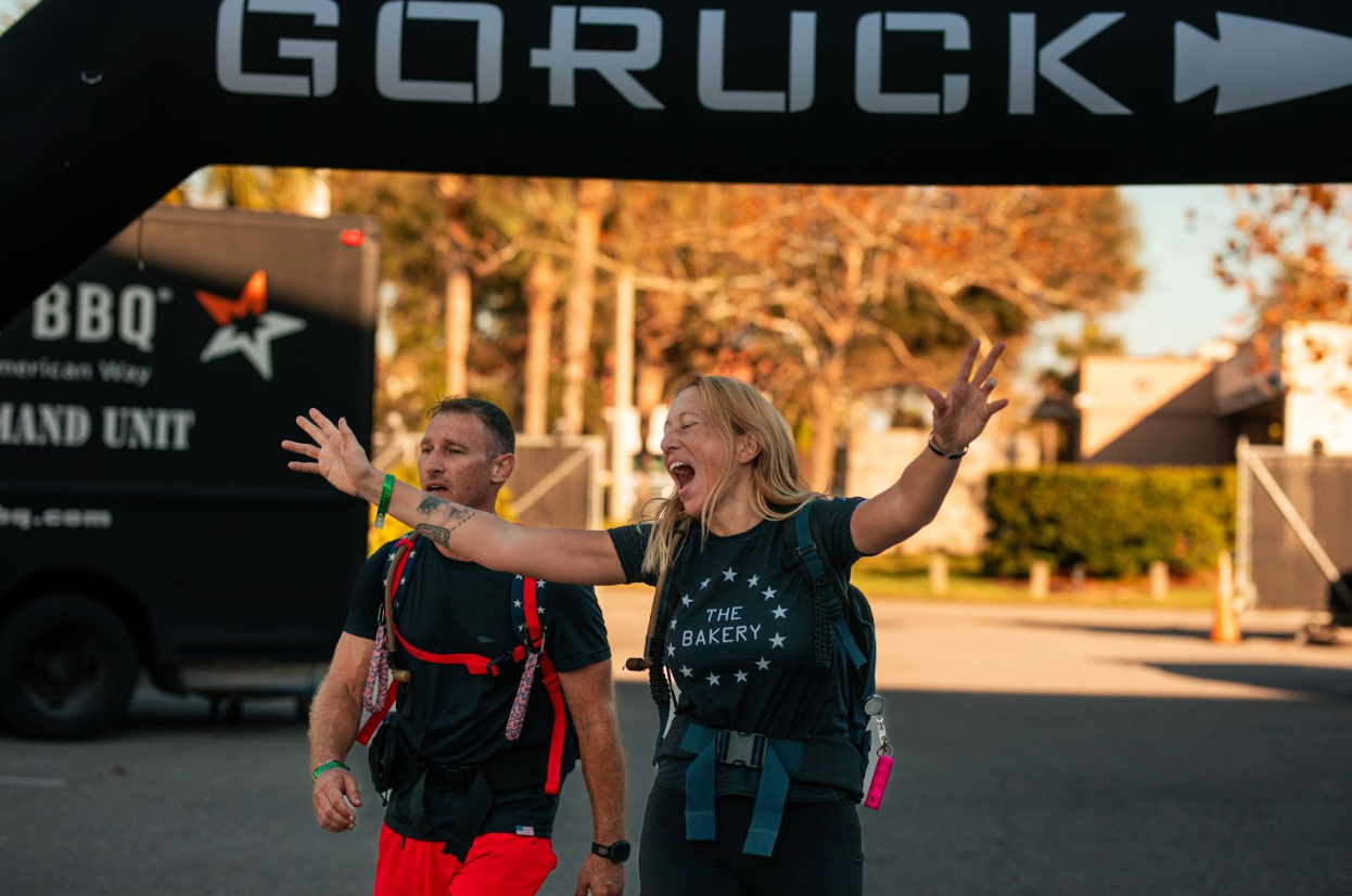 Two ruckers celebrating at a GORUCK event finish line, wearing rucking gear outdoors.