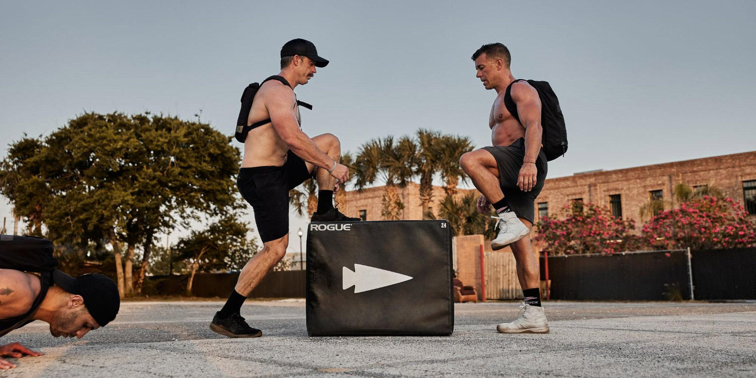Men training outdoors with GORUCK gear, performing box jumps and pushups in urban setting