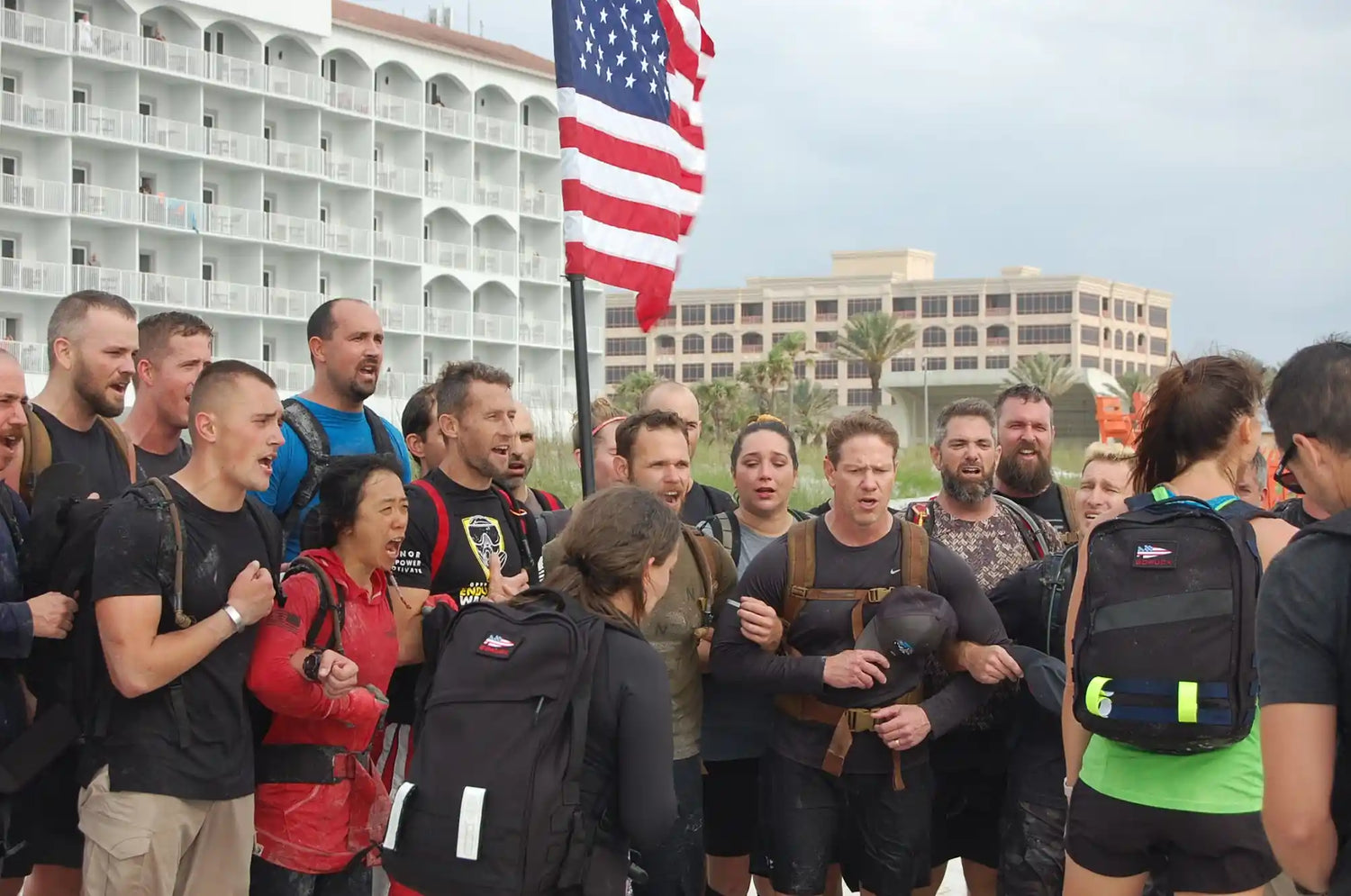 Group of GORUCK participants with rucksacks and American flag at outdoor event