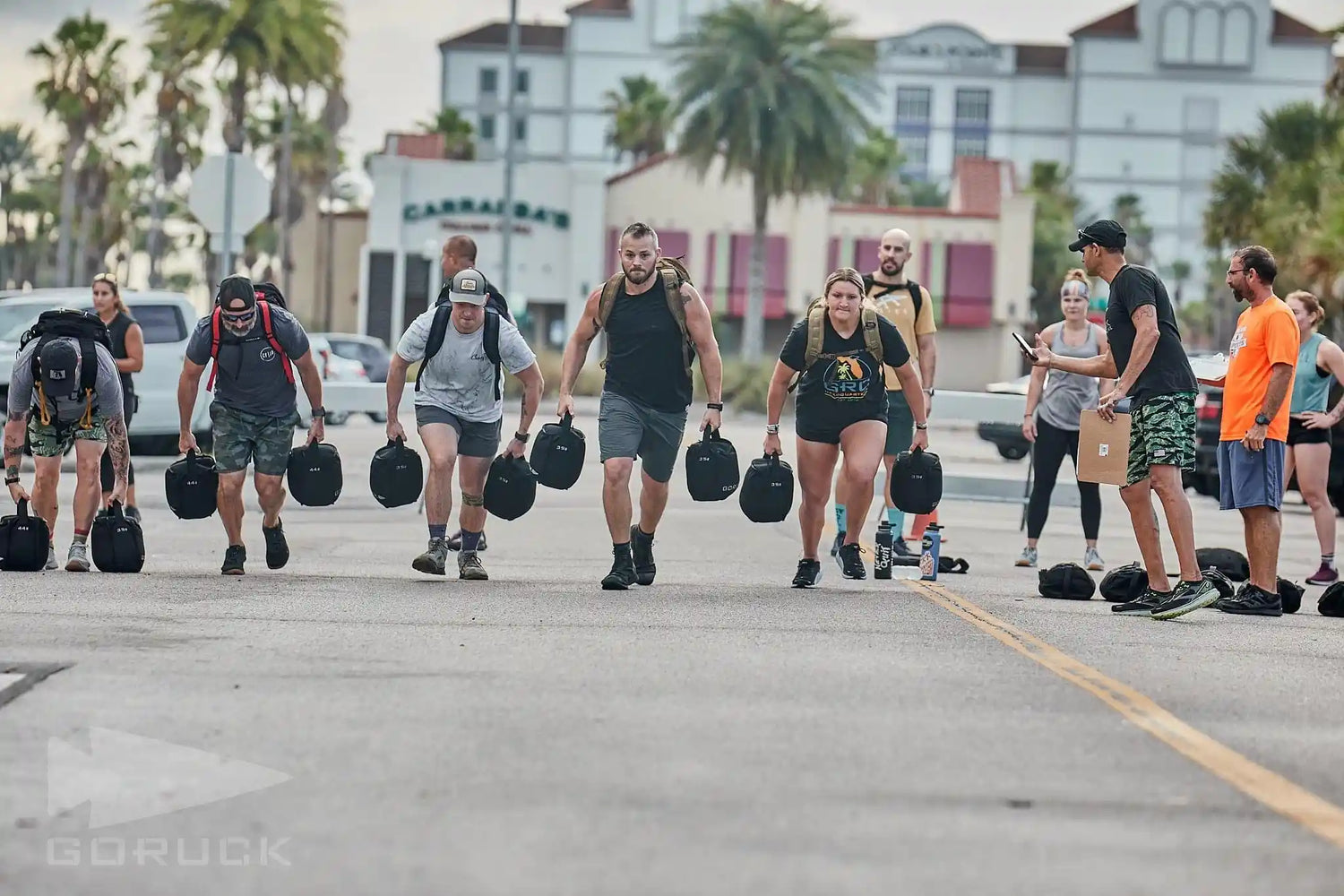 Group of people rucking with weighted bags on a street during a GORUCK fitness event