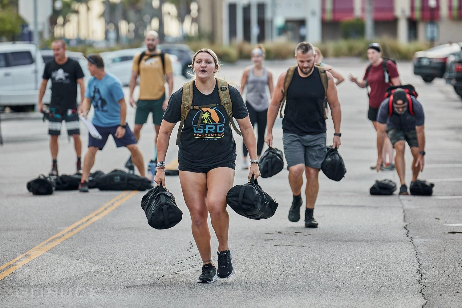 Group rucking workout with GORUCK gear on city street, people carrying sandbags and backpacks