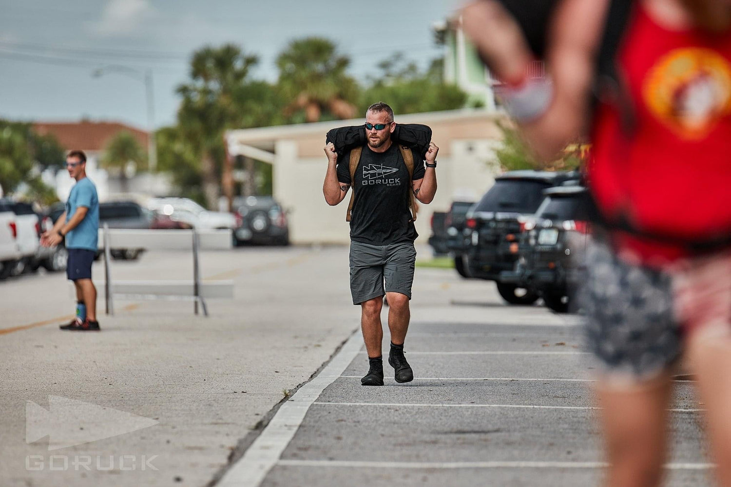 Man wearing GORUCK gear rucking with a sandbag on his shoulders during outdoor event