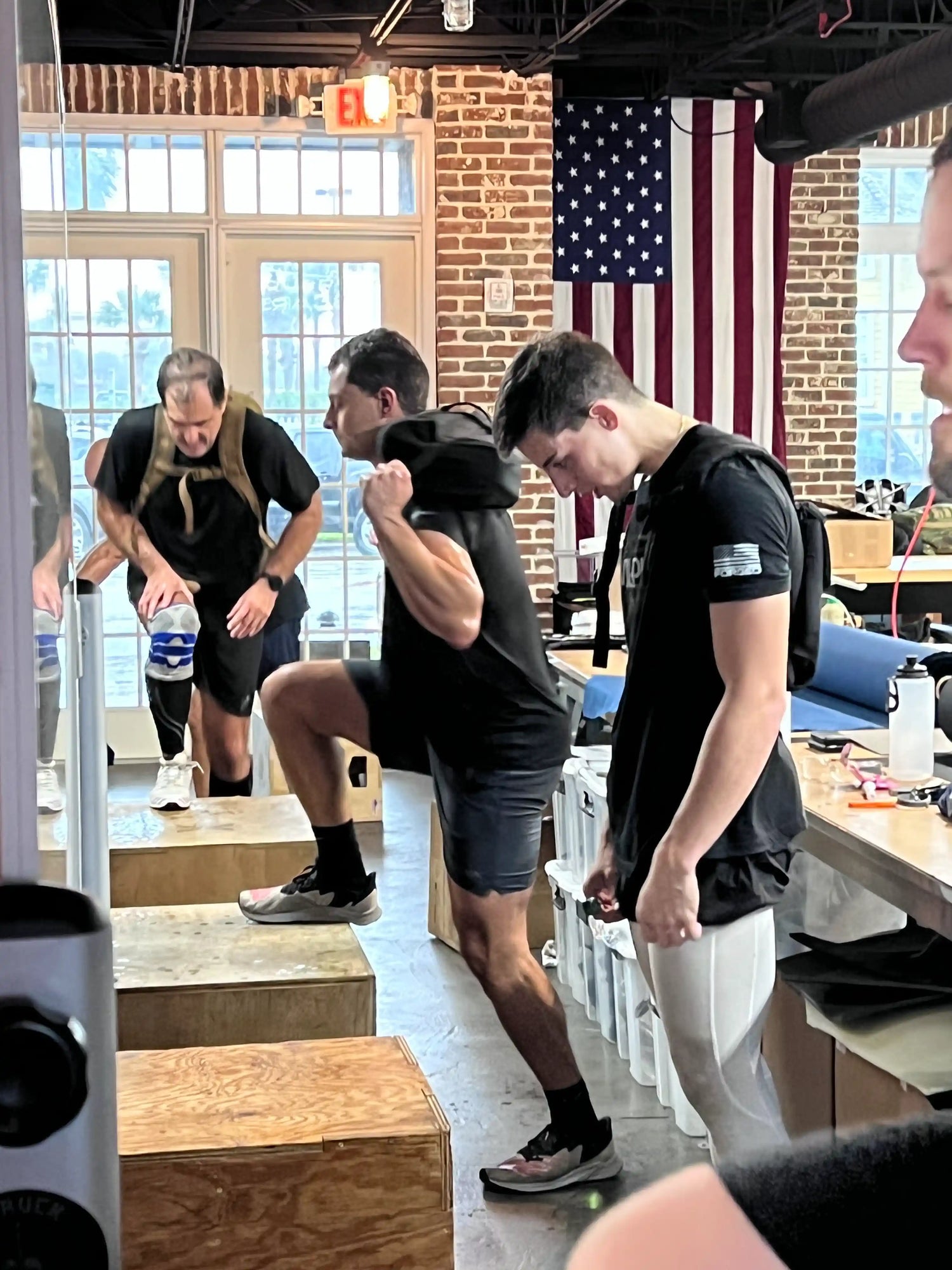 Group training with GORUCK rucksacks in gym, American flag background, box step exercise
