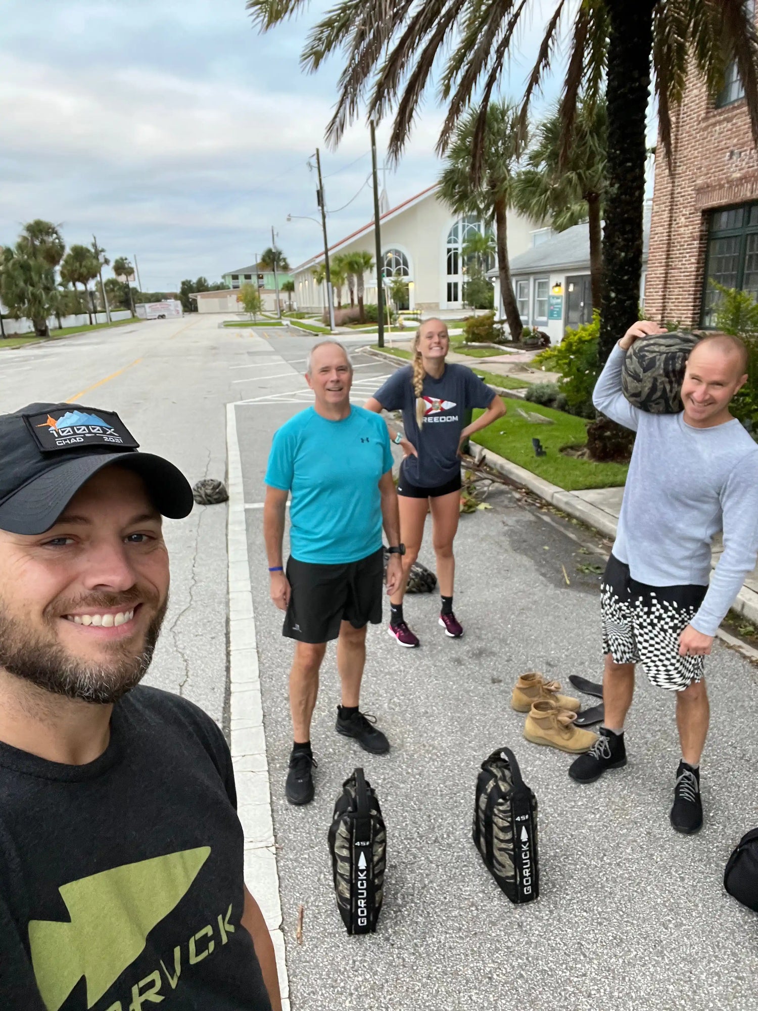 GORUCK team smiling outdoors with rucking gear and sandbags on a palm-lined street