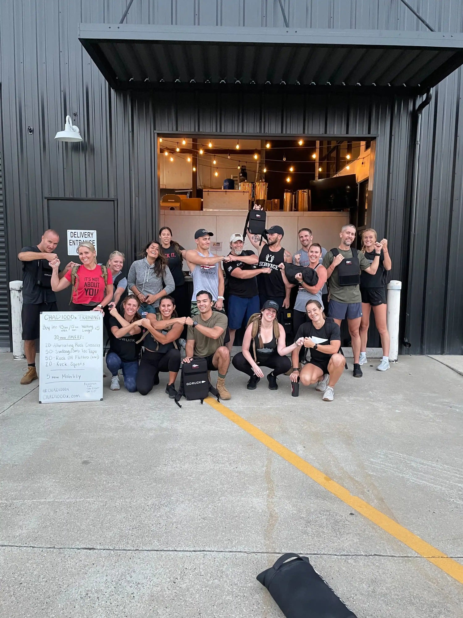 Group of people in athletic gear posing outside GORUCK facility, showing rucking equipment
