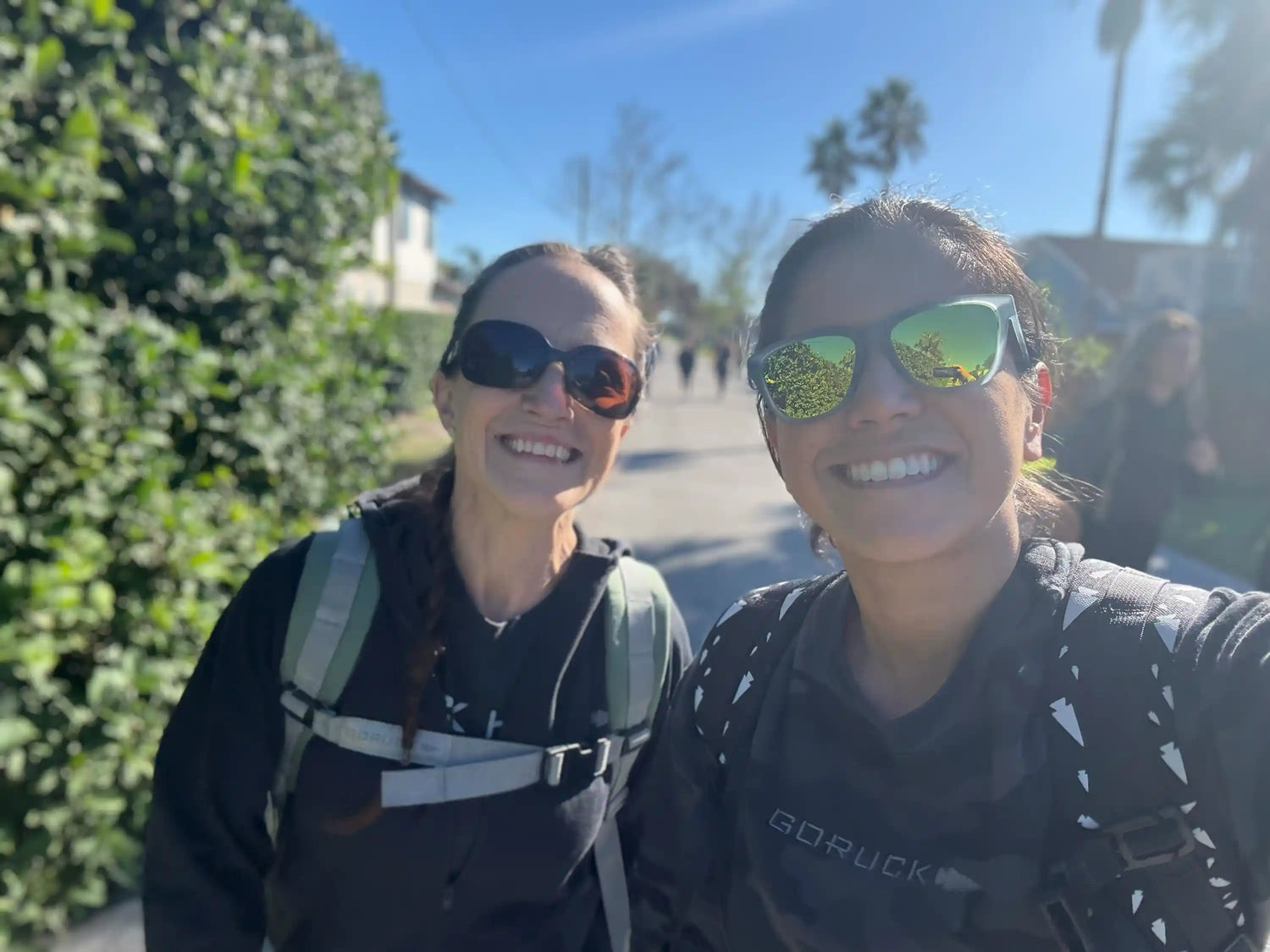 Two women in sunglasses wearing GORUCK gear smiling outdoors on a sunny day.