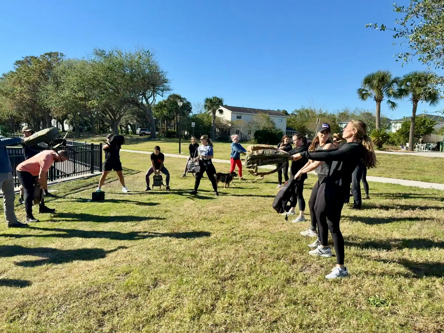 Group rucking workout outside, people swinging GORUCK backpacks on sunny lawn