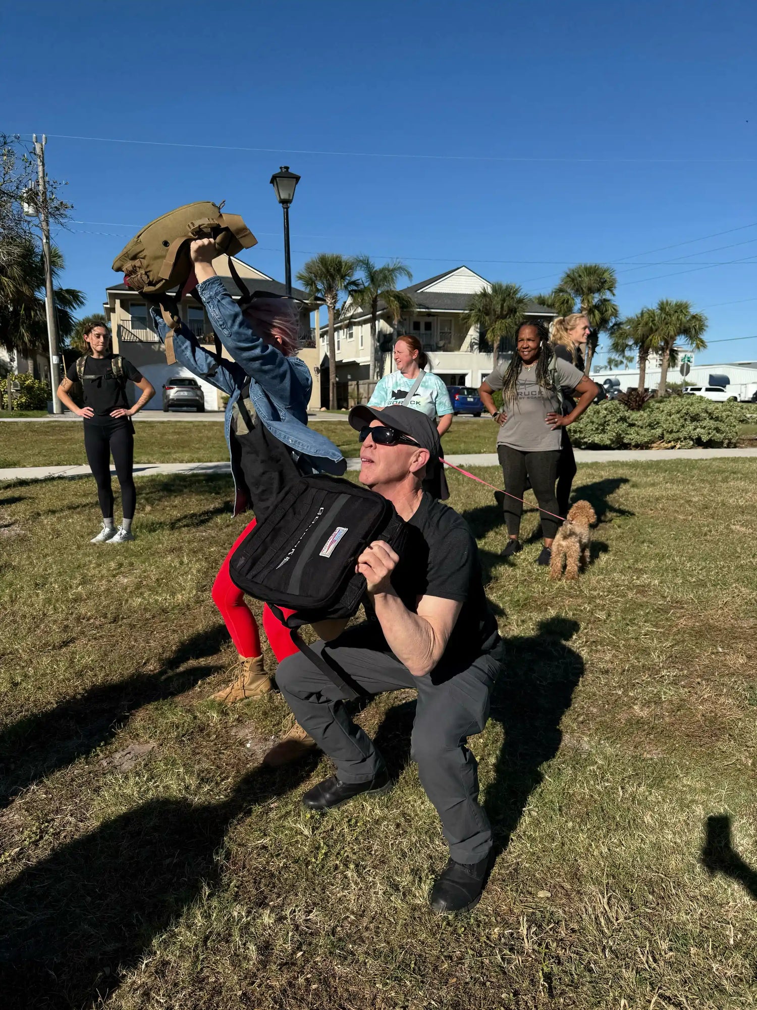 Group outdoor rucking workout with GORUCK gear, people exercising on grass under blue sky