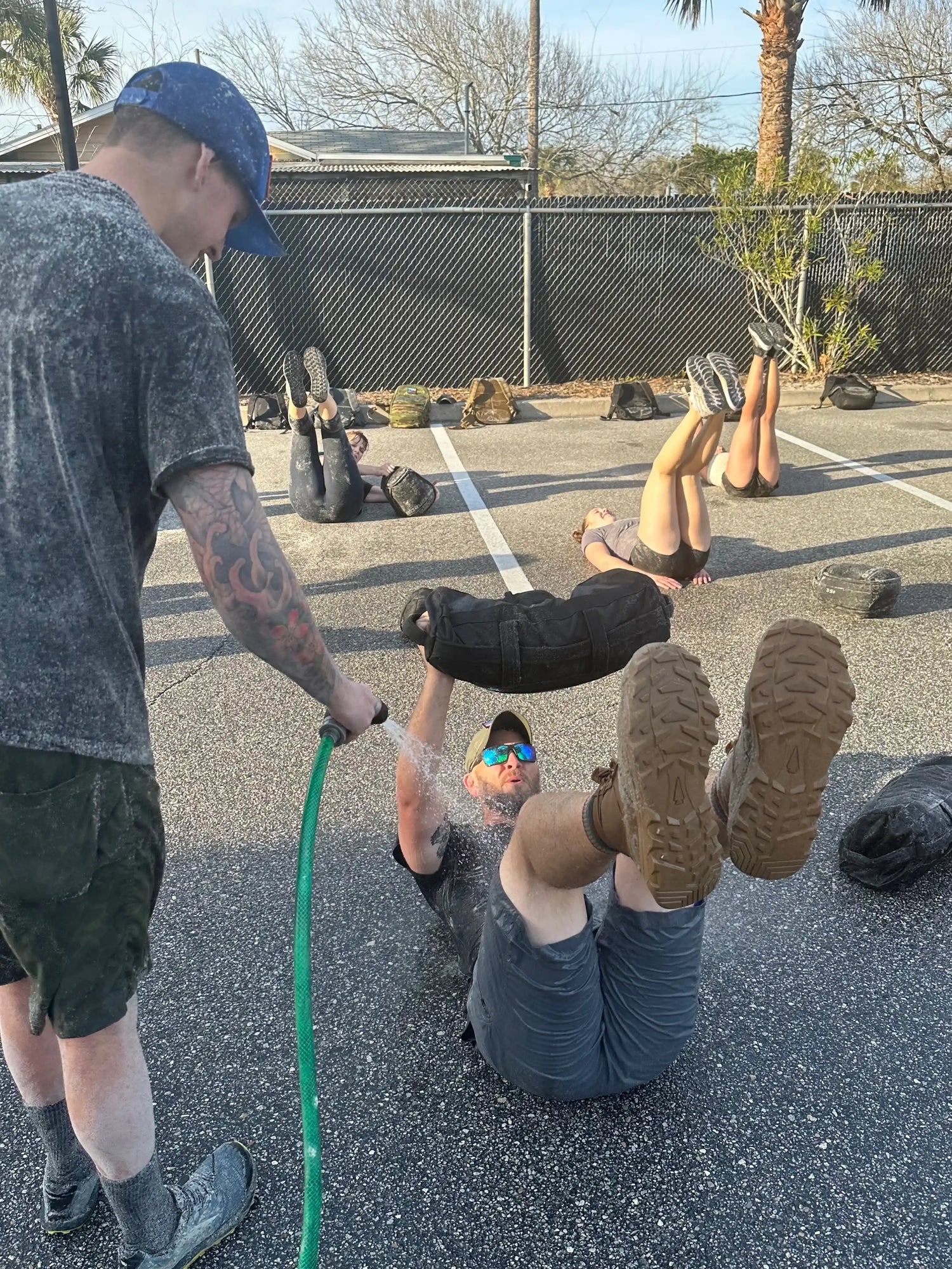 GORUCK outdoor fitness training, participants doing exercises with rucksacks, water hose spray