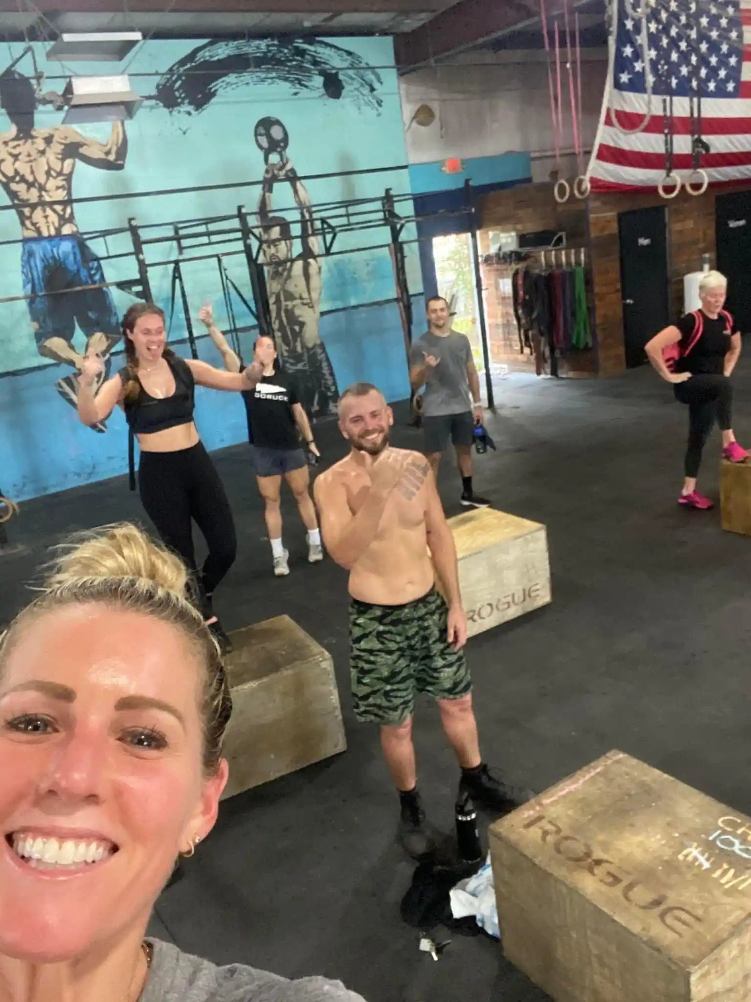 Group fitness class at GORUCK gym with athletes posing by ROGUE boxes under American flag