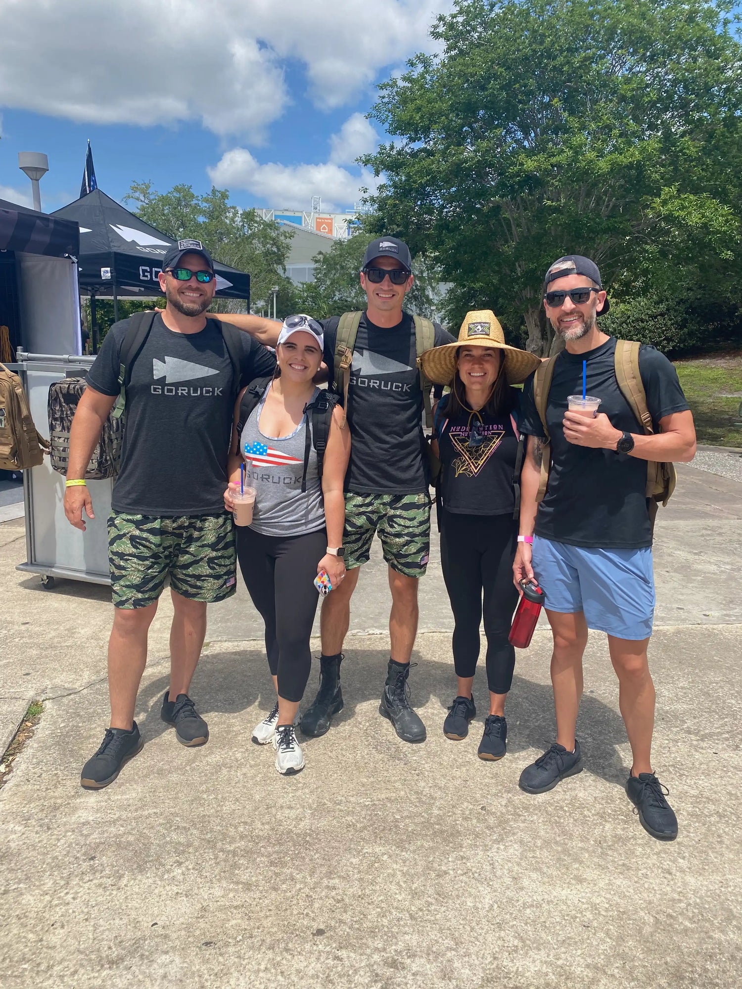 Group of five people in GORUCK gear outdoors at an event, with tents and trees in background