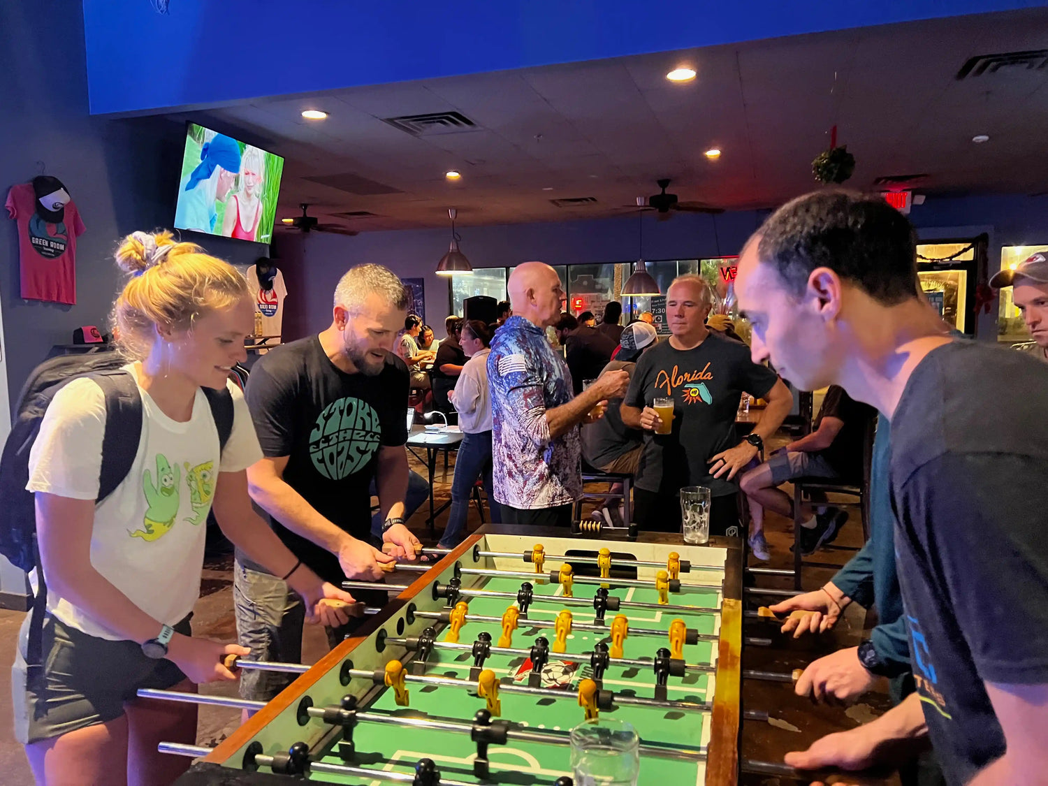 Group playing foosball in a bar, GORUCK shirts, lively social atmosphere