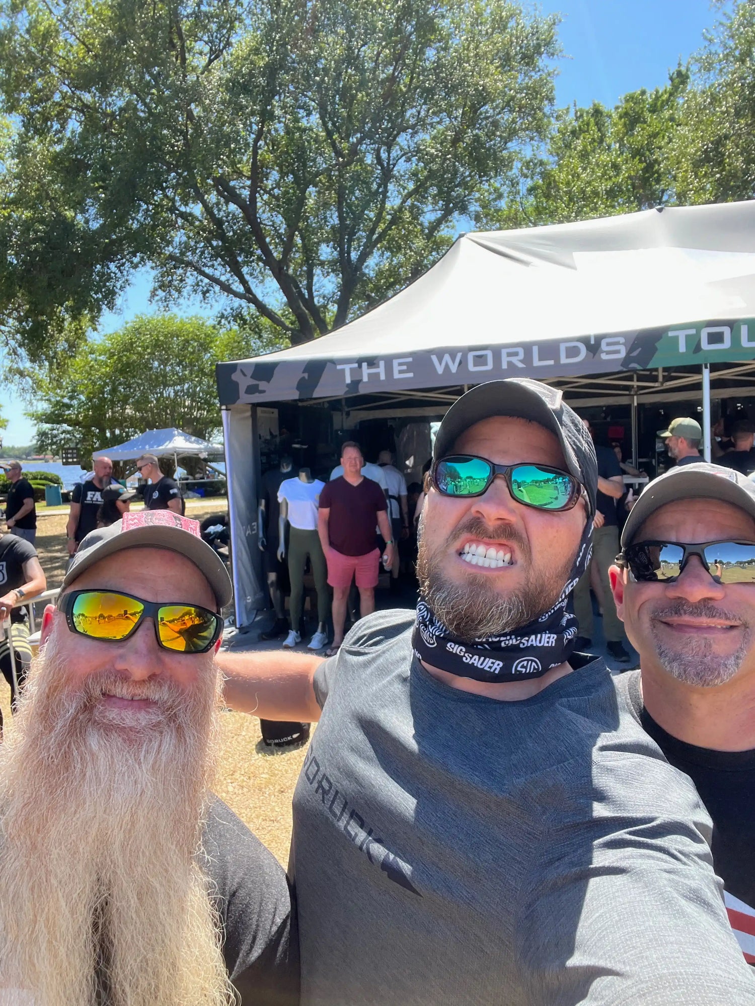 Group of men at GORUCK outdoor event in front of branded tent, wearing sunglasses and gear.