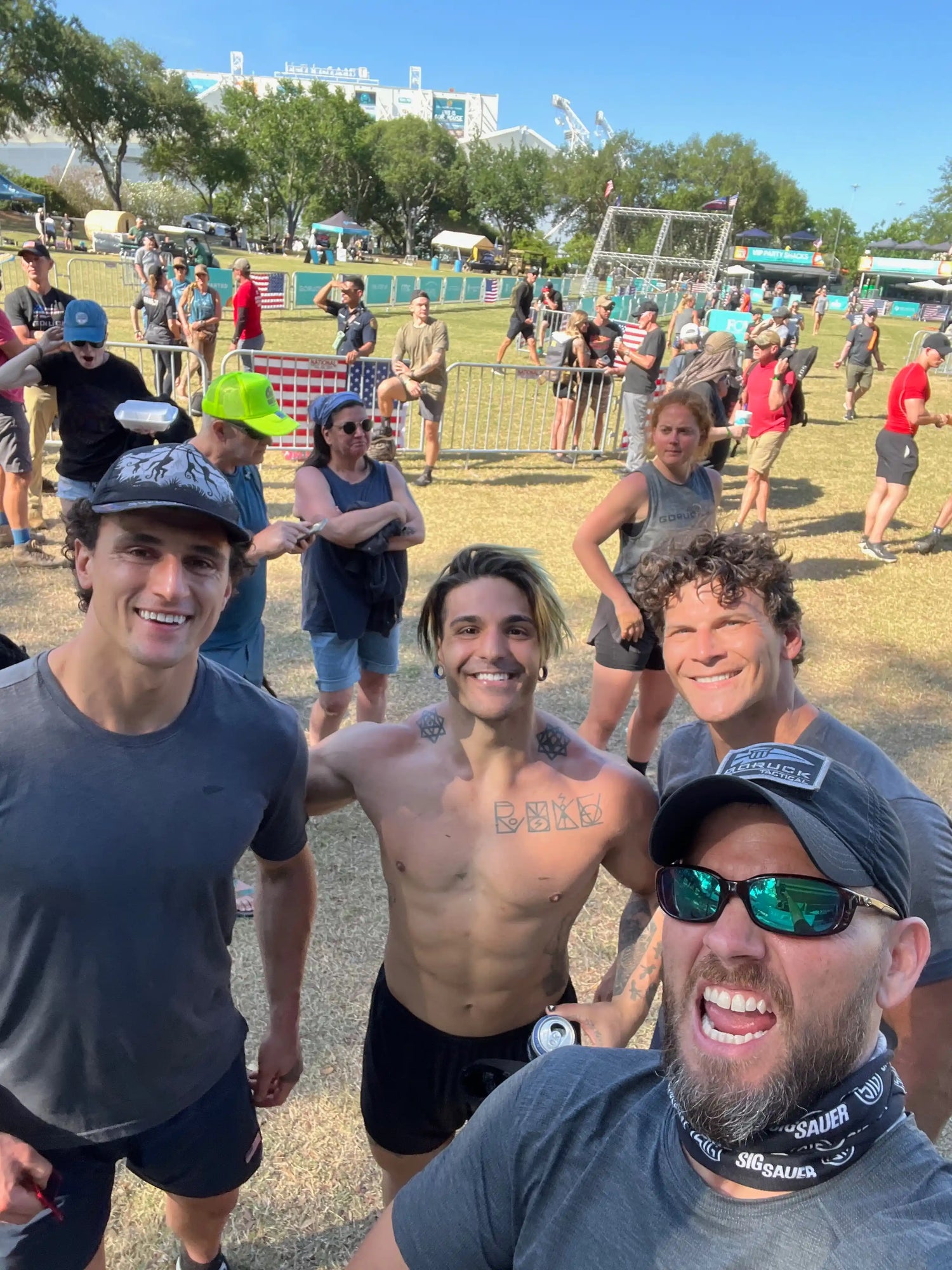 Group of smiling athletes at GORUCK outdoor rucking event, people and obstacle setup in background
