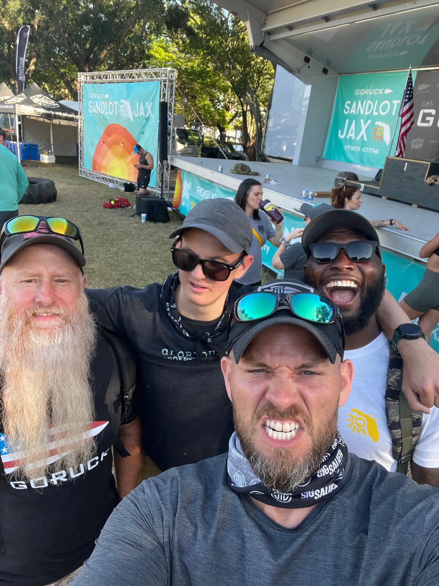 Group of people at GORUCK Sandlot JAX fitness festival outdoors with event banners and stage