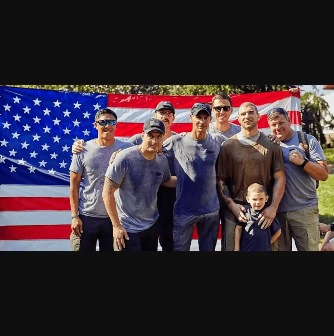 GORUCK team in wet athletic gear posing in front of a large American flag outdoors