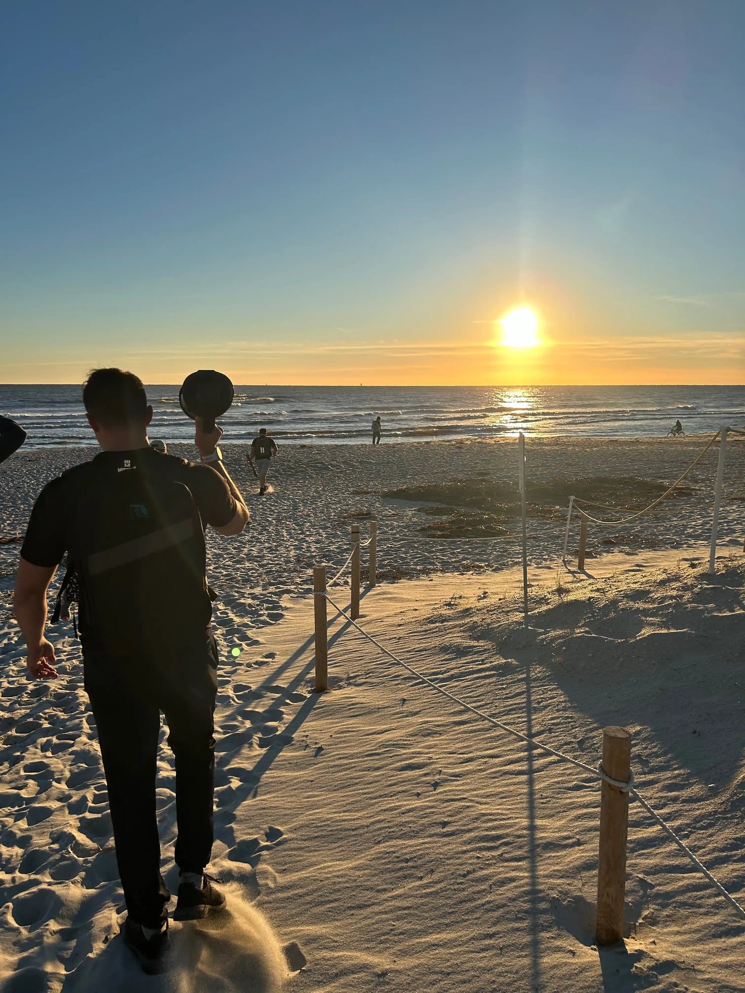 GORUCK athlete carrying weight on sandy beach at sunset, training by the ocean