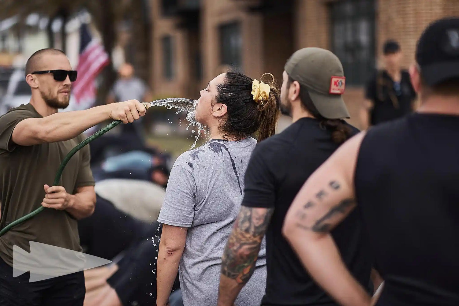GORUCK event participants hydrating with a hose outdoors, American flag in background