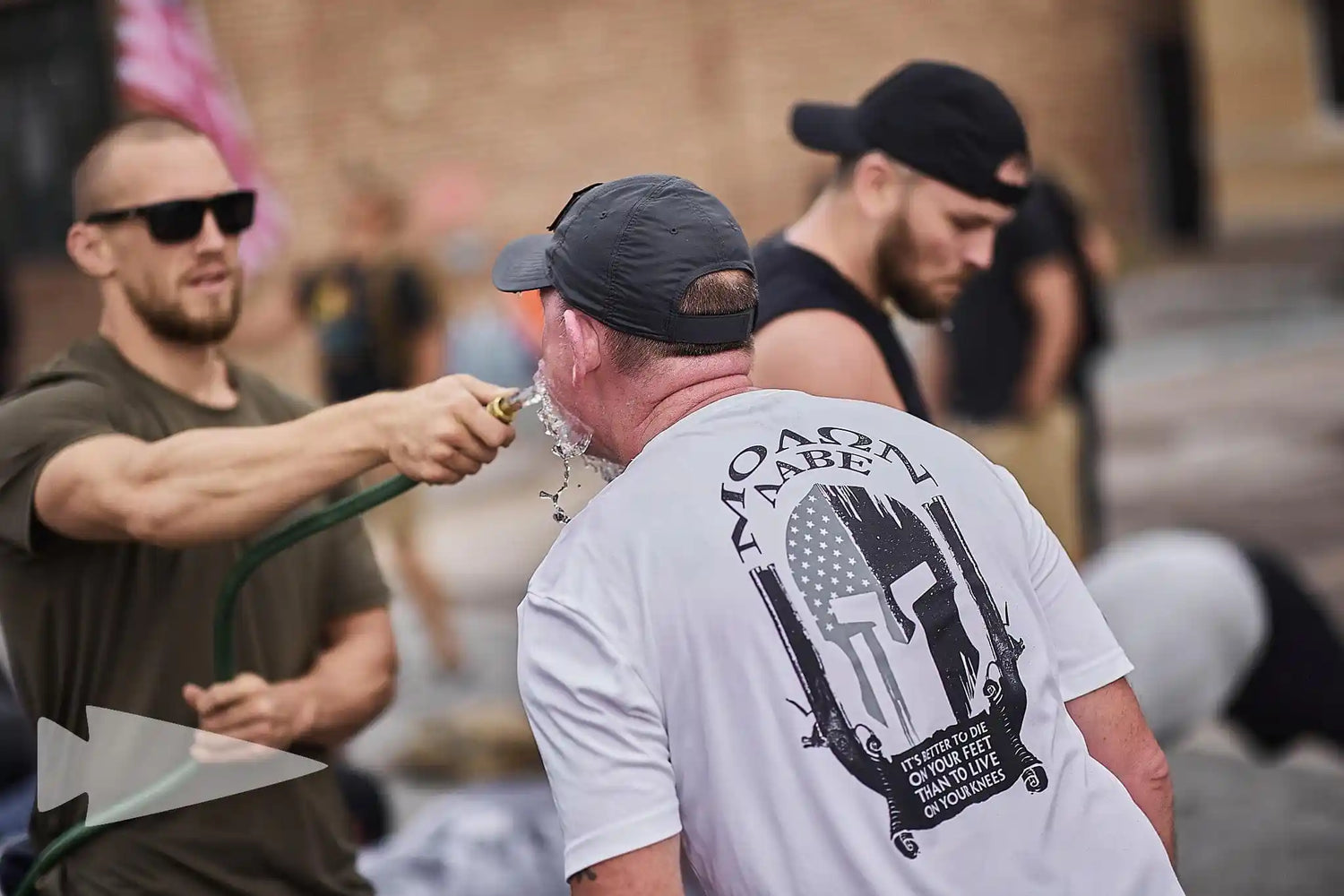 GORUCK participants during outdoor rucking event, man rinsing face with water hose, teamwork focus