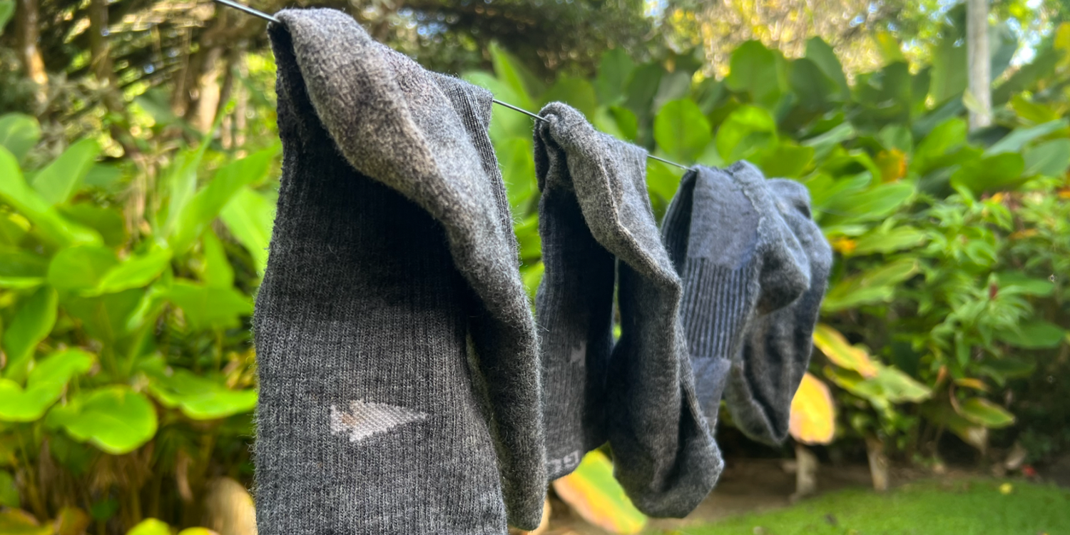 Gray merino wool socks drying on a line outdoors with green foliage in the background