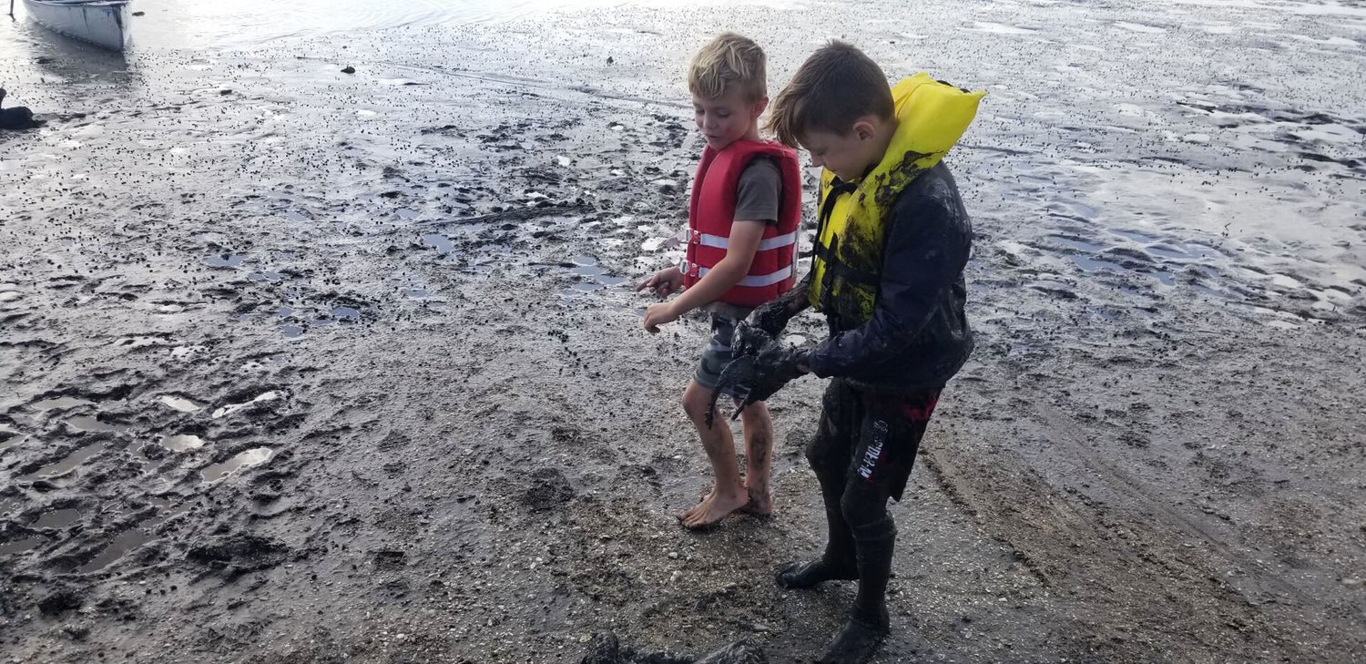 Two boys in life jackets playing in muddy shoreline, GORUCK tough outdoor adventure gear