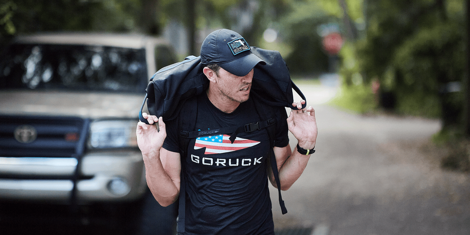 Man rucking outdoors wearing GORUCK gear and hat, carrying weight on shoulders on a street
