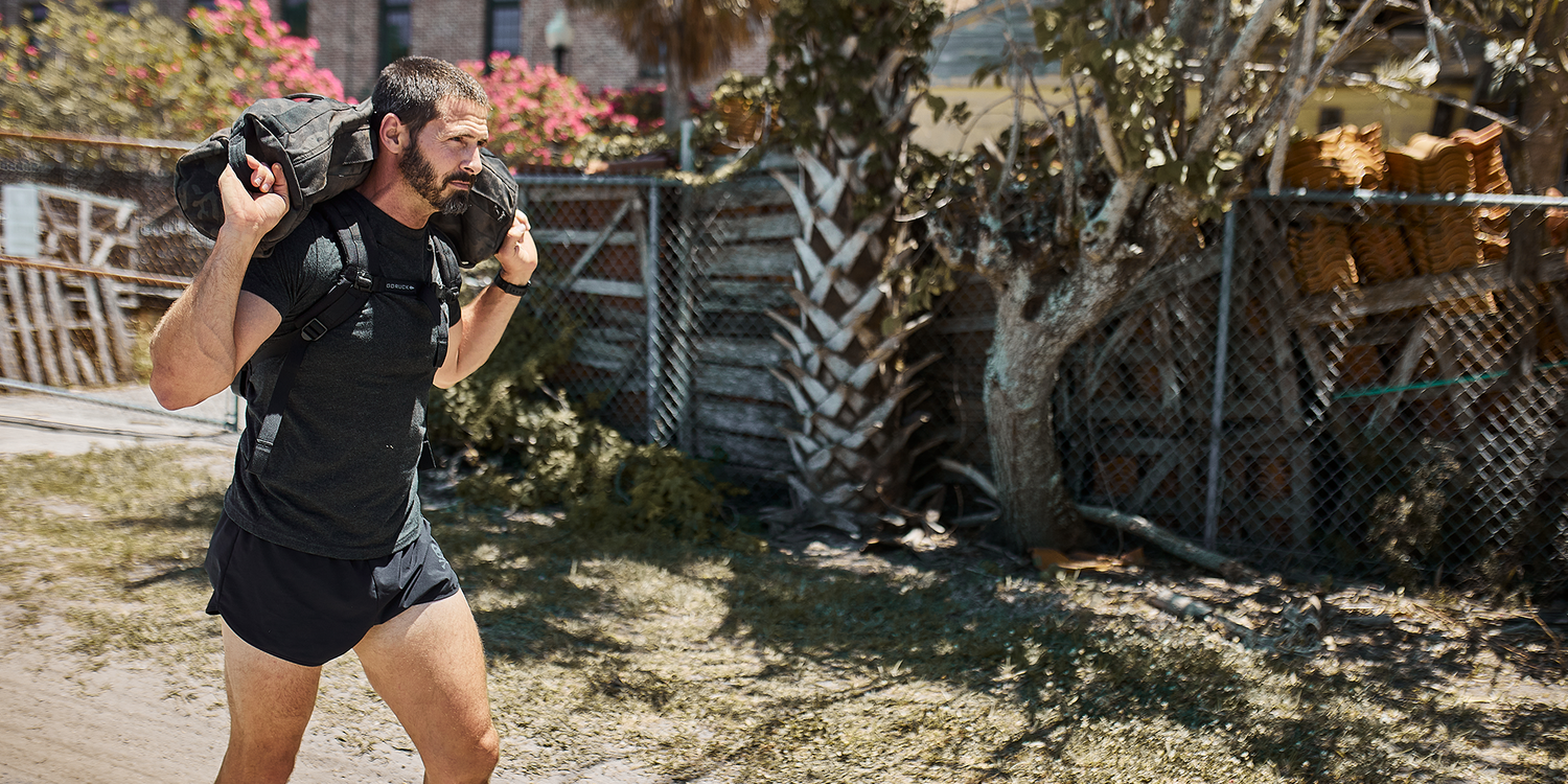 Man rucking outdoors in GORUCK gear and running shorts, carrying weighted backpack
