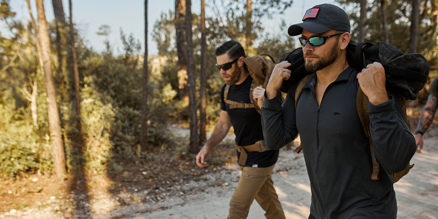 Two men rucking with weighted packs in a forest, wearing GORUCK gear and sunglasses.