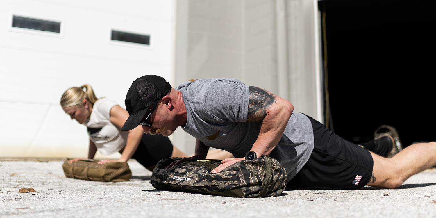 Two people doing outdoor sandbag push-ups with GORUCK rucking gear