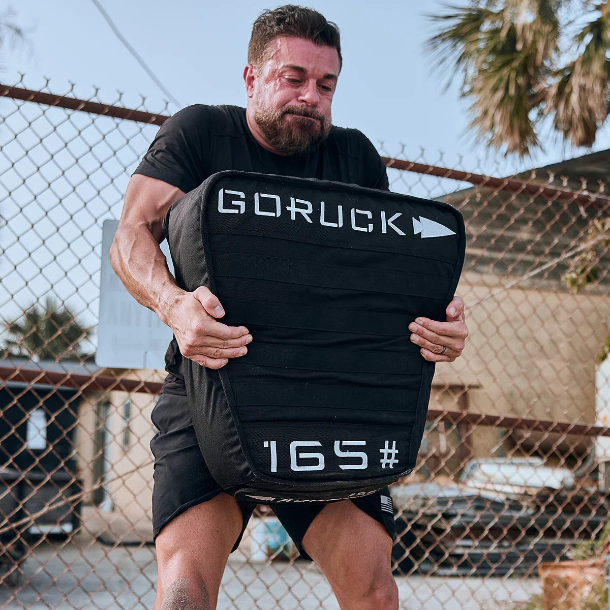 Man lifting GORUCK 165 lb sandbag outdoors, showcasing rugged rucking fitness gear