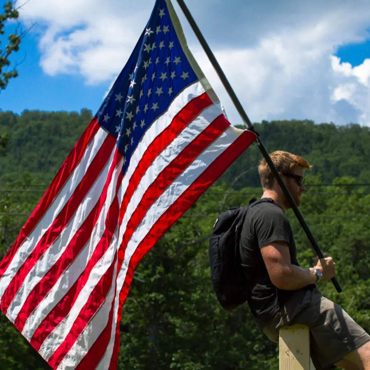 Man with backpack holding American flag outdoors, GORUCK rucking gear in action