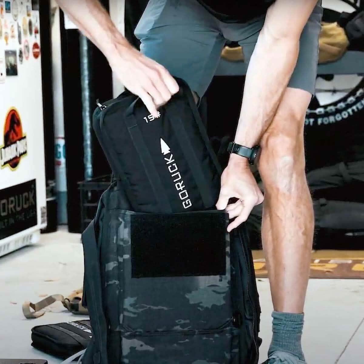 Man loading a GORUCK 15lb sand plate into a tactical rucksack for rucking gear training