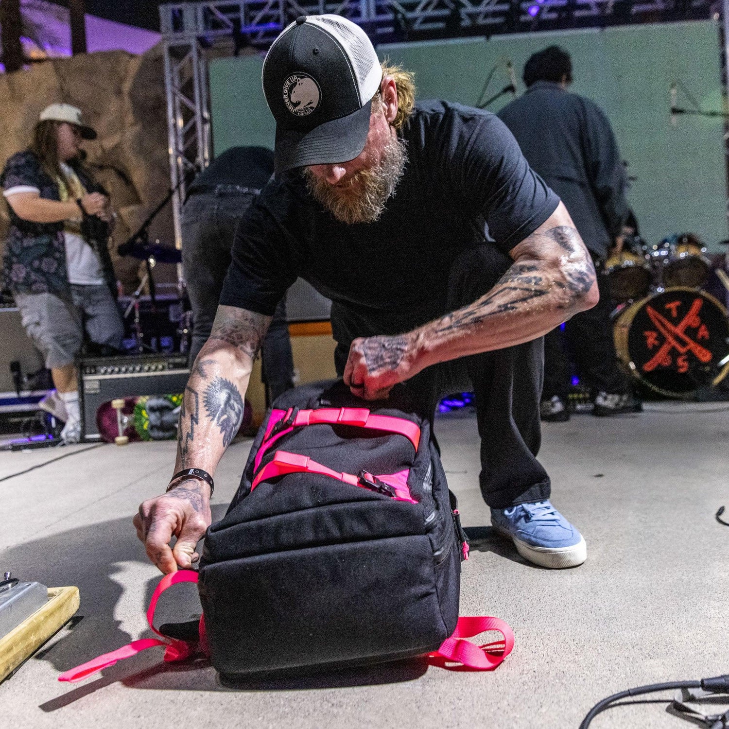 Tattooed man kneeling and packing black GORUCK rucksack with red straps at event stage