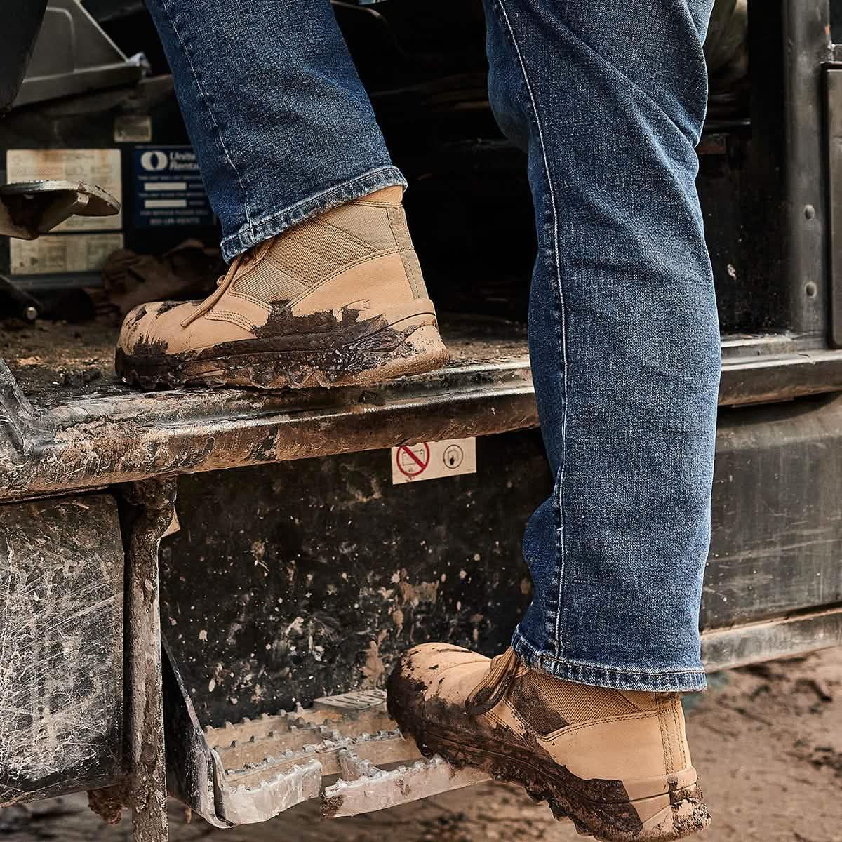 Person wearing tan GORUCK rucking boots with mud, stepping onto a truck in rugged outdoor setting