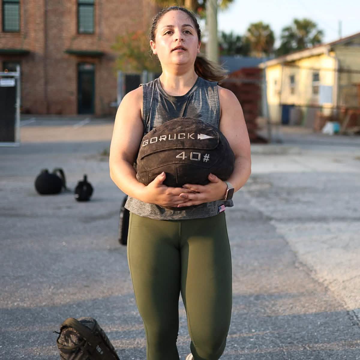 Woman outdoors holding GORUCK 40 lb sandbag, wearing athletic gear, rucking training