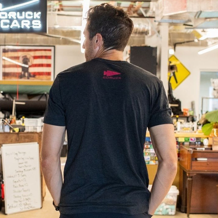 A person stands in a workshop, facing away with hands in pockets; a Rule 1 sign is visible.