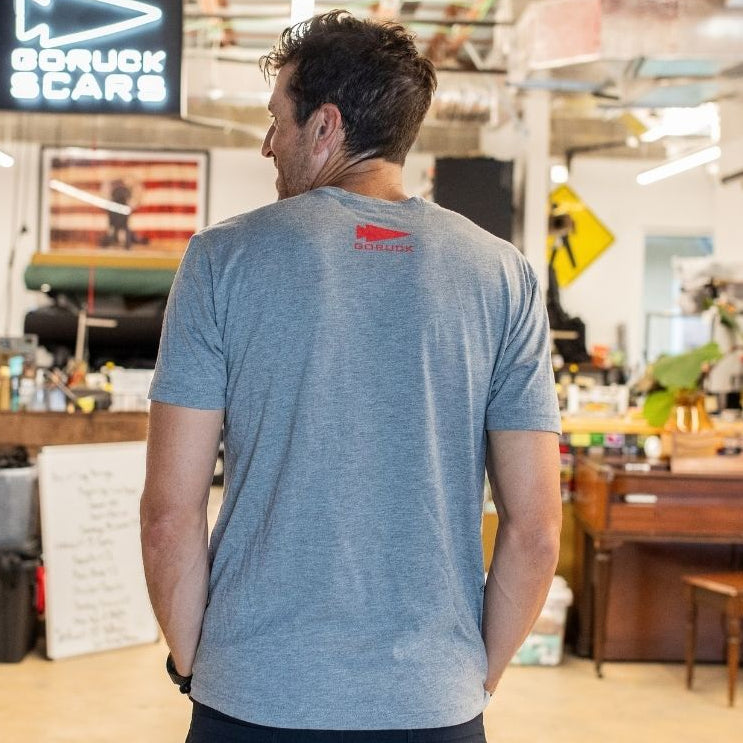 A man wearing the Graphic T-Shirt - 100% American stands with his back to the camera in a cluttered workshop space.