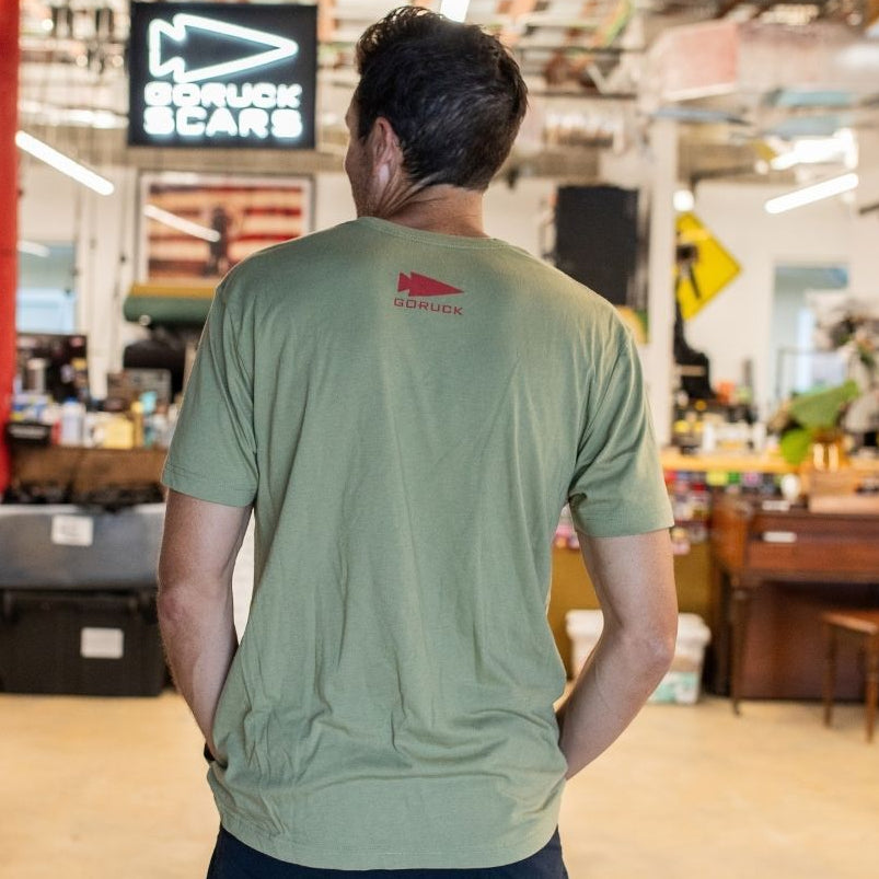 Wearing an AmeRUCKa green t-shirt, a person stands in a spacious, well-lit workshop with their back to the camera.