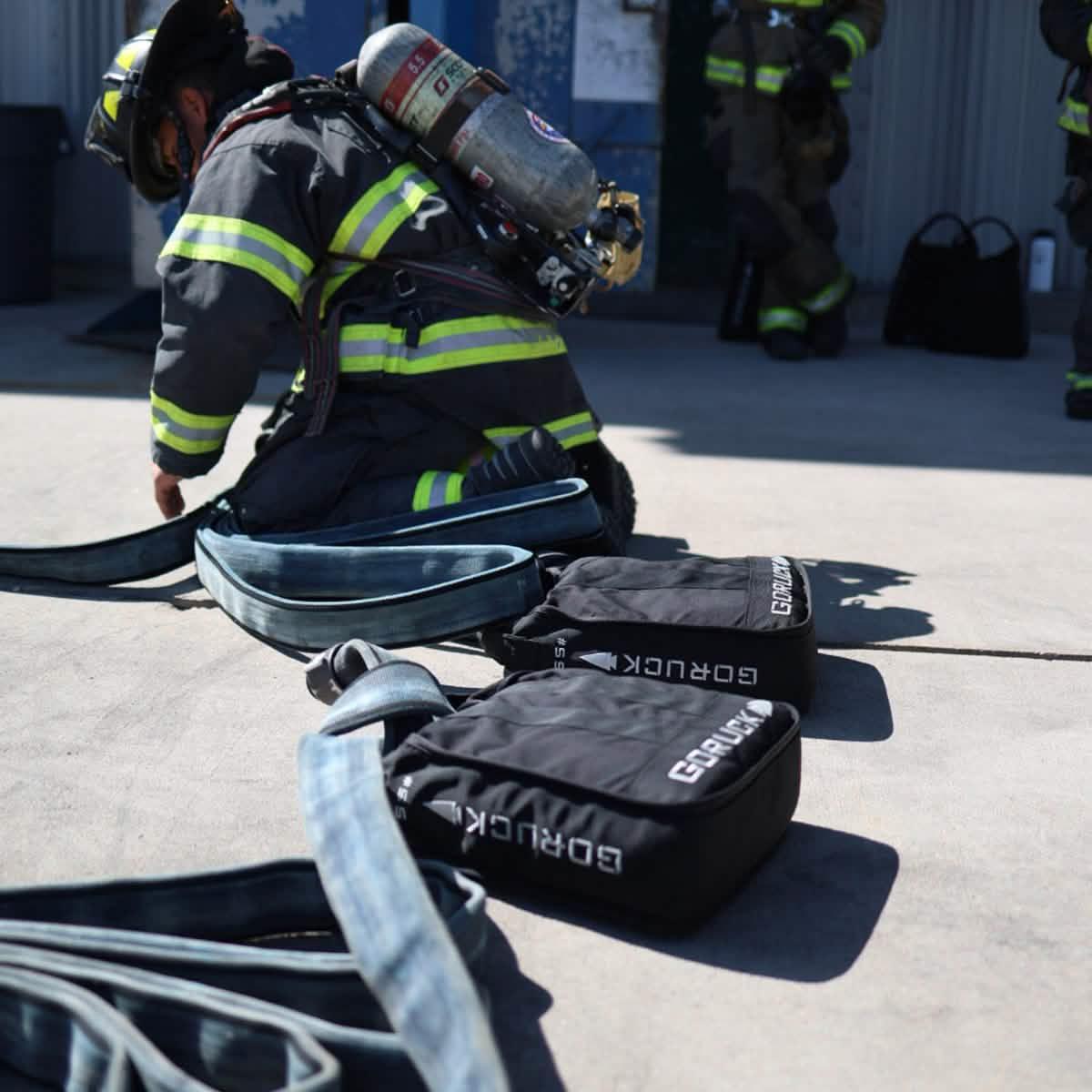 Firefighter in gear next to GORUCK rucking bags and fire hoses outdoors