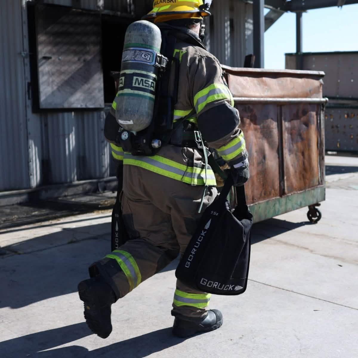 Firefighter carrying GORUCK rucking gear near a dumpster outdoors