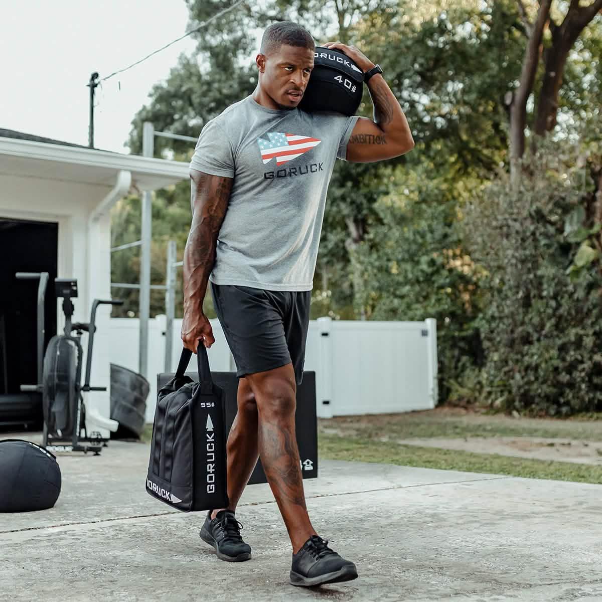 Man rucking outdoors with GORUCK sandbag and weight, wearing GORUCK gear in backyard gym