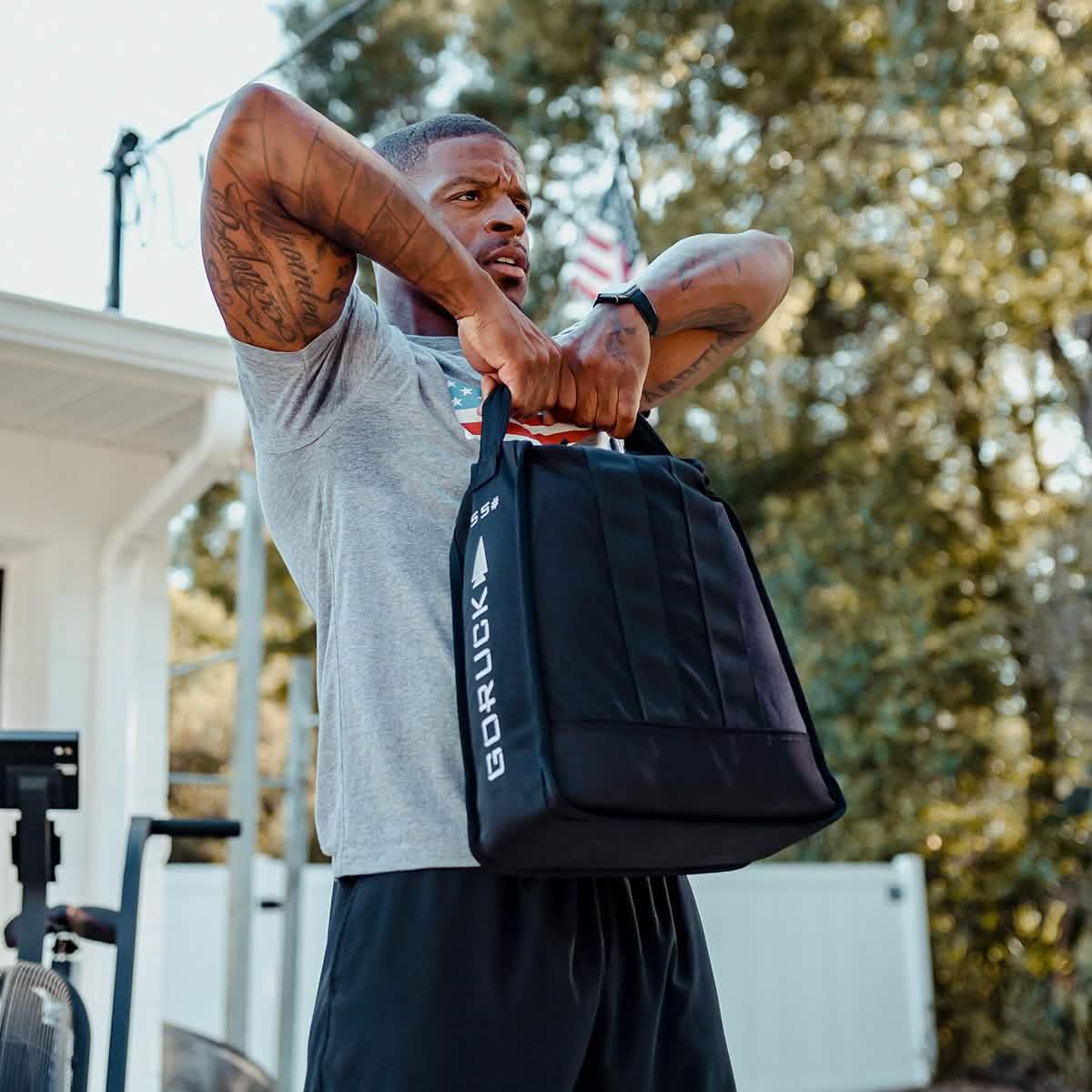 Man exercising outdoors with GORUCK weighted training bag, American flag in background