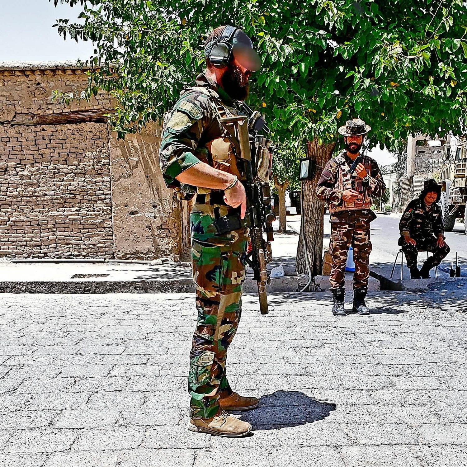 Men in tactical gear and camouflage stand outdoors by brick building and trees, demonstrating GORUCK rugged rucking equipment.