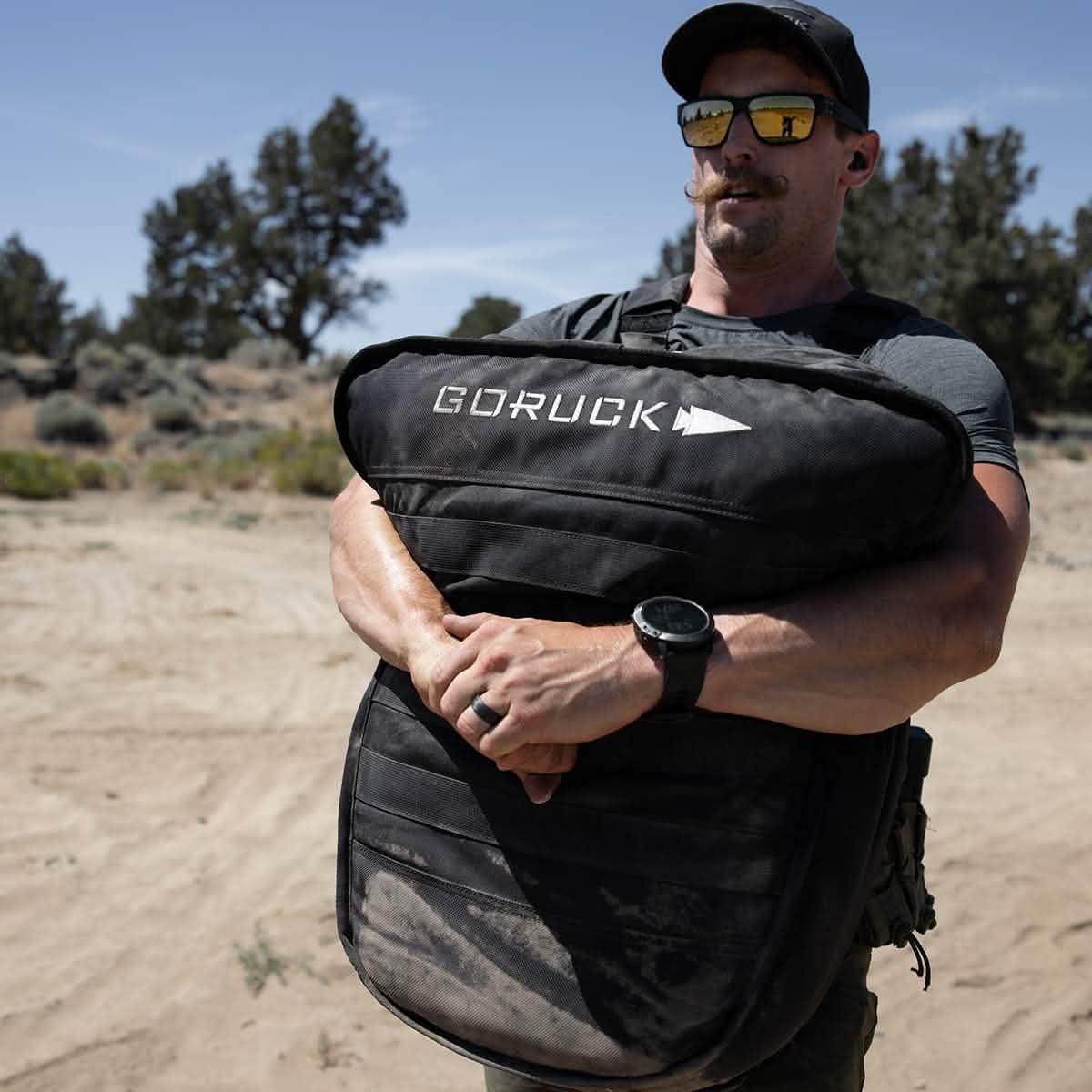Man outdoors carrying large GORUCK rucking sandbag, wearing sunglasses and athletic gear