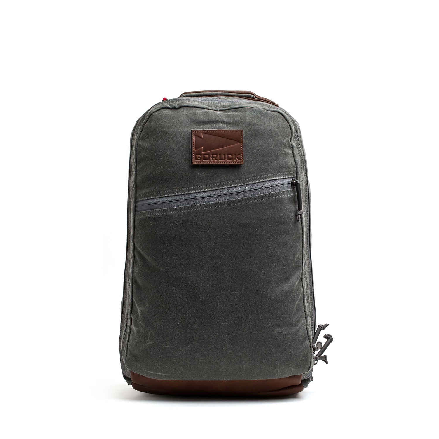 The Double Compartment Bullet Ruck - Heritage Waxed Canvas - 18L is a gray backpack with a brown leather patch and bottom, plus a diagonal front zipper pocket—ideal as a stylish travel daypack.